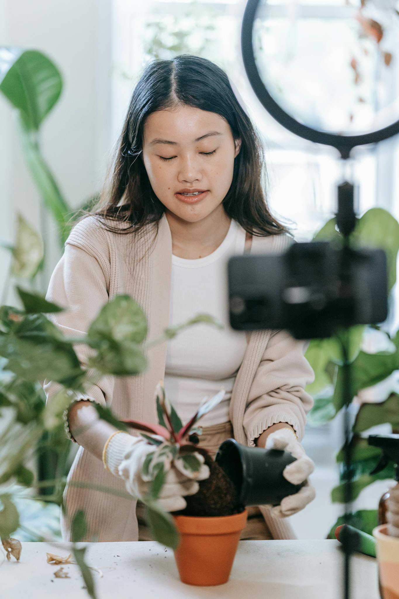 Asian woman vlogging about indoor plant care, using a camera and ring light.